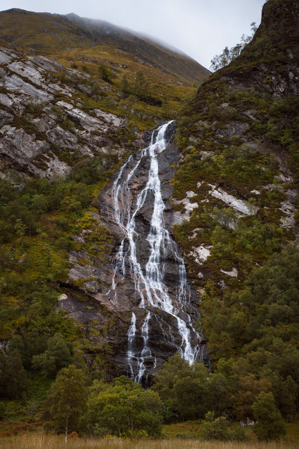 Steall Falls pours over a large rock face in several large streams before dissapearing into the trees below
