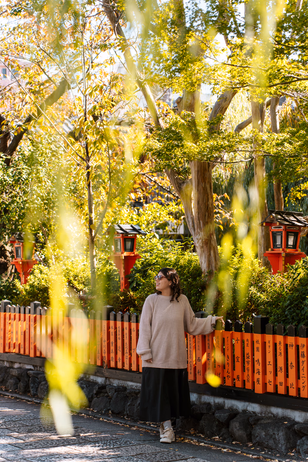 A woman leans on an orange fence in the Gion neighbourhood in Kyoto, Japan