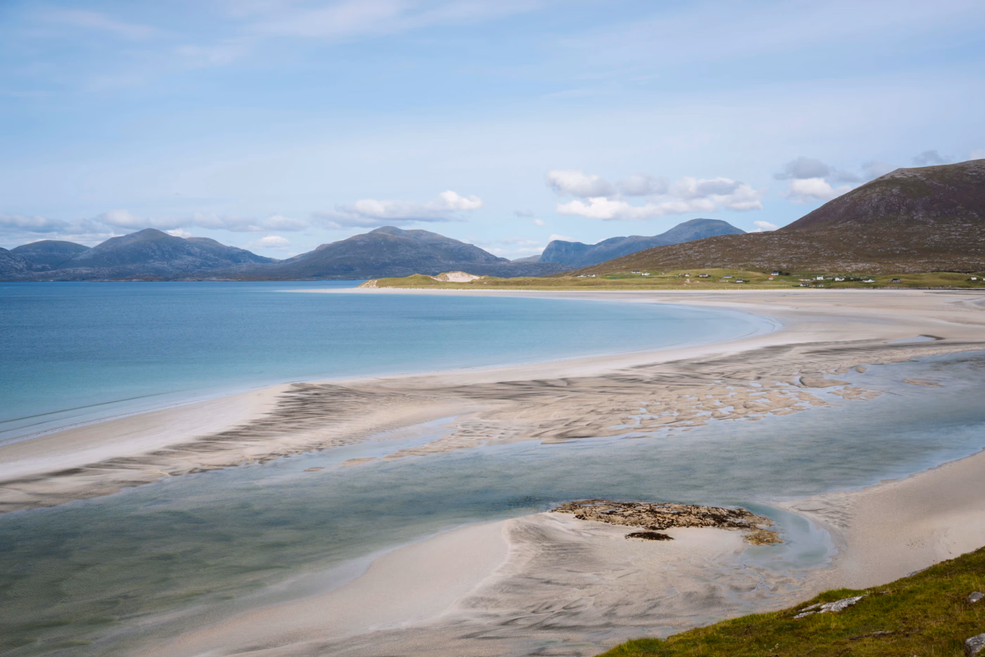 Rolling hills in the distance and white sand exposed by a low tide on a ideal beach on the Isle of Lewis and Harris