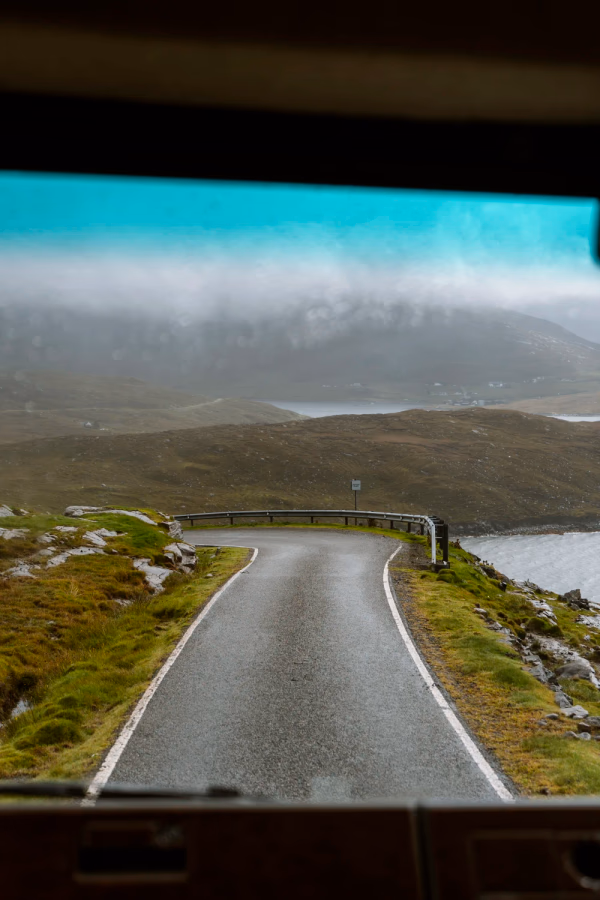 A narrow single track road disappears around the corner framed through the windshield. ofa car