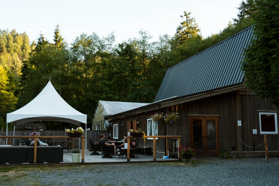 several people lounging around the patio furniture outside a renovated old brown barn at a Cidery on Bowen Island, BC