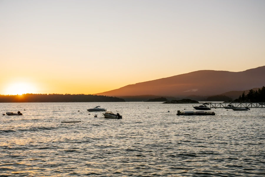 Sunset behind a distant island covered in trees while anchored motor boats bob in the water in the foreground