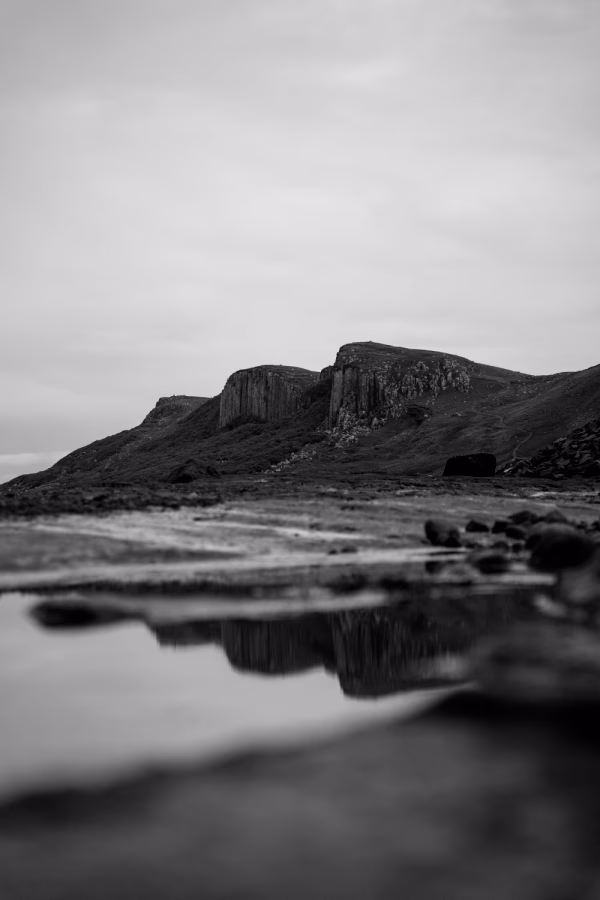 Distant mountains are reflected in a shallow tide pool on Corran Beach on The Isle of Skye, Scotland