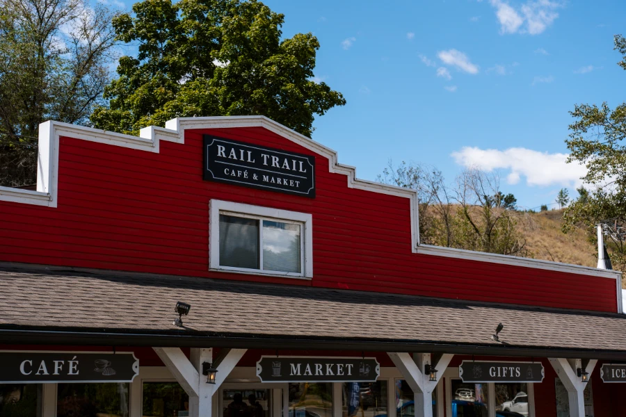 A Red wood-panel facade with a sign reading ‘Rail Trail Cafe & Market’ is supported by several white wooden pillars