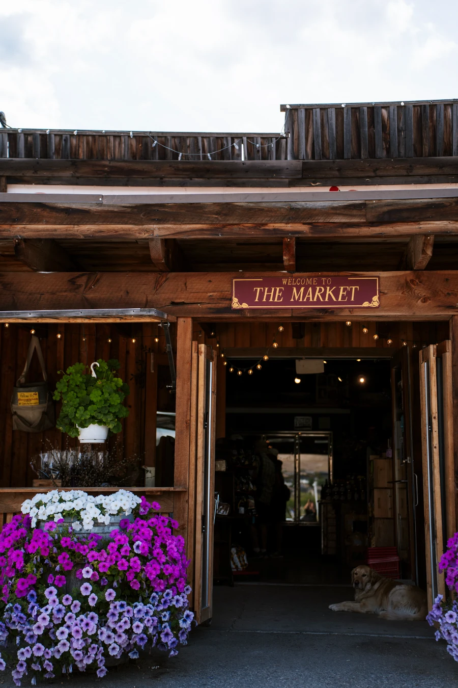 A wooden archway with large flower pots on either end leads into a building with a sign hanging over it that reads ‘The Market’