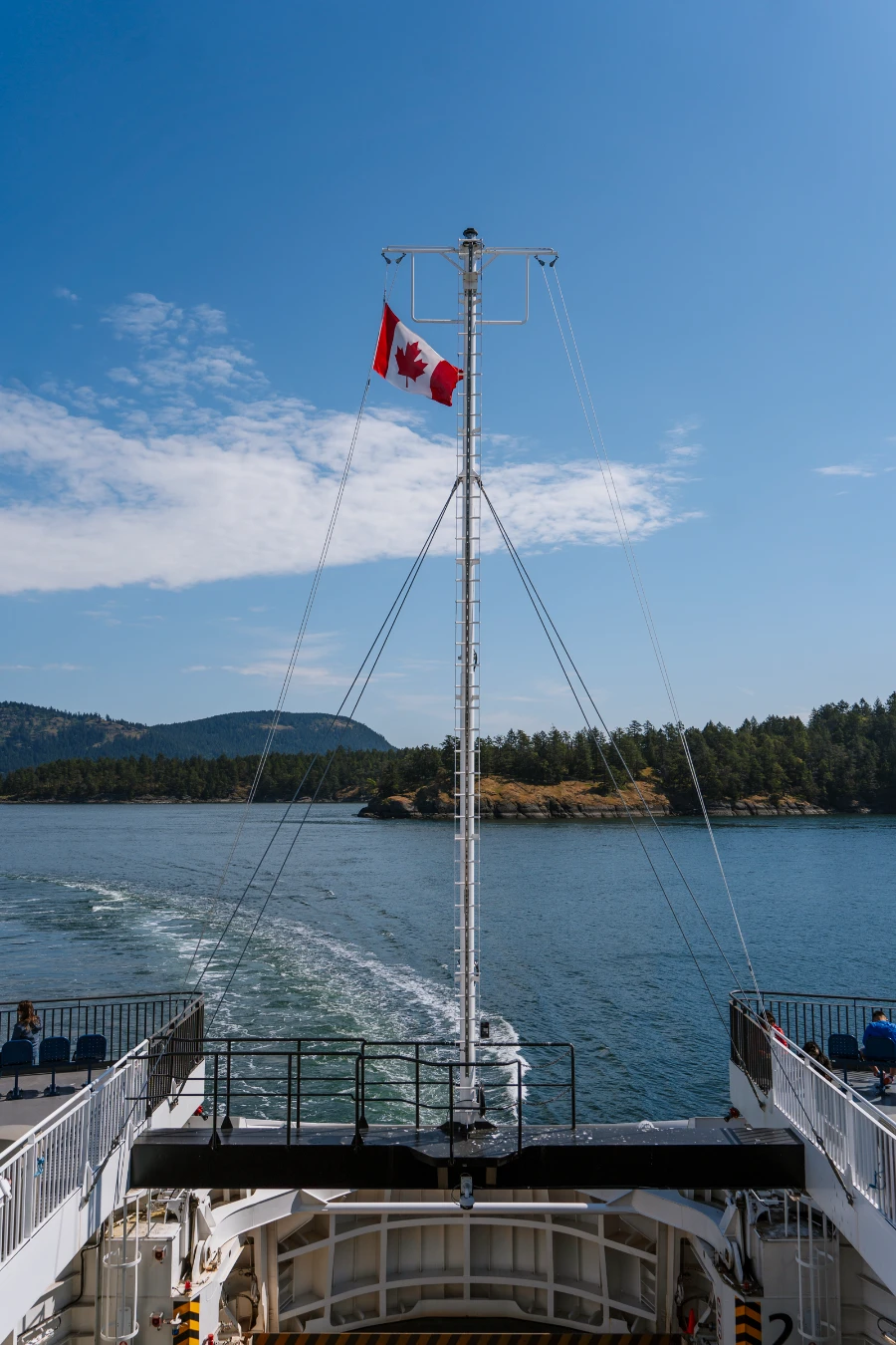 A Canadian flag blow is the wind on board a BC ferry that is leaving a strong wake behind it