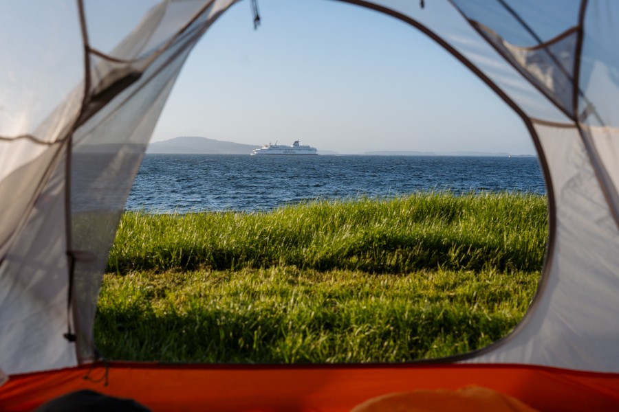 A BC ferries navigating between golf islands framed through the front flap of a tent