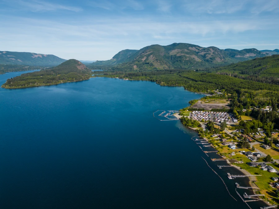 A deep blue lake lined with lush green rolling hills and shores lined with floating log barriers