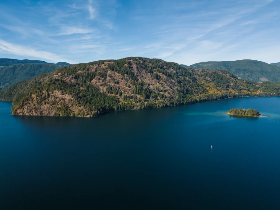A deep blue lake with a round mountain behind it, with bald stony patches and patches with trees