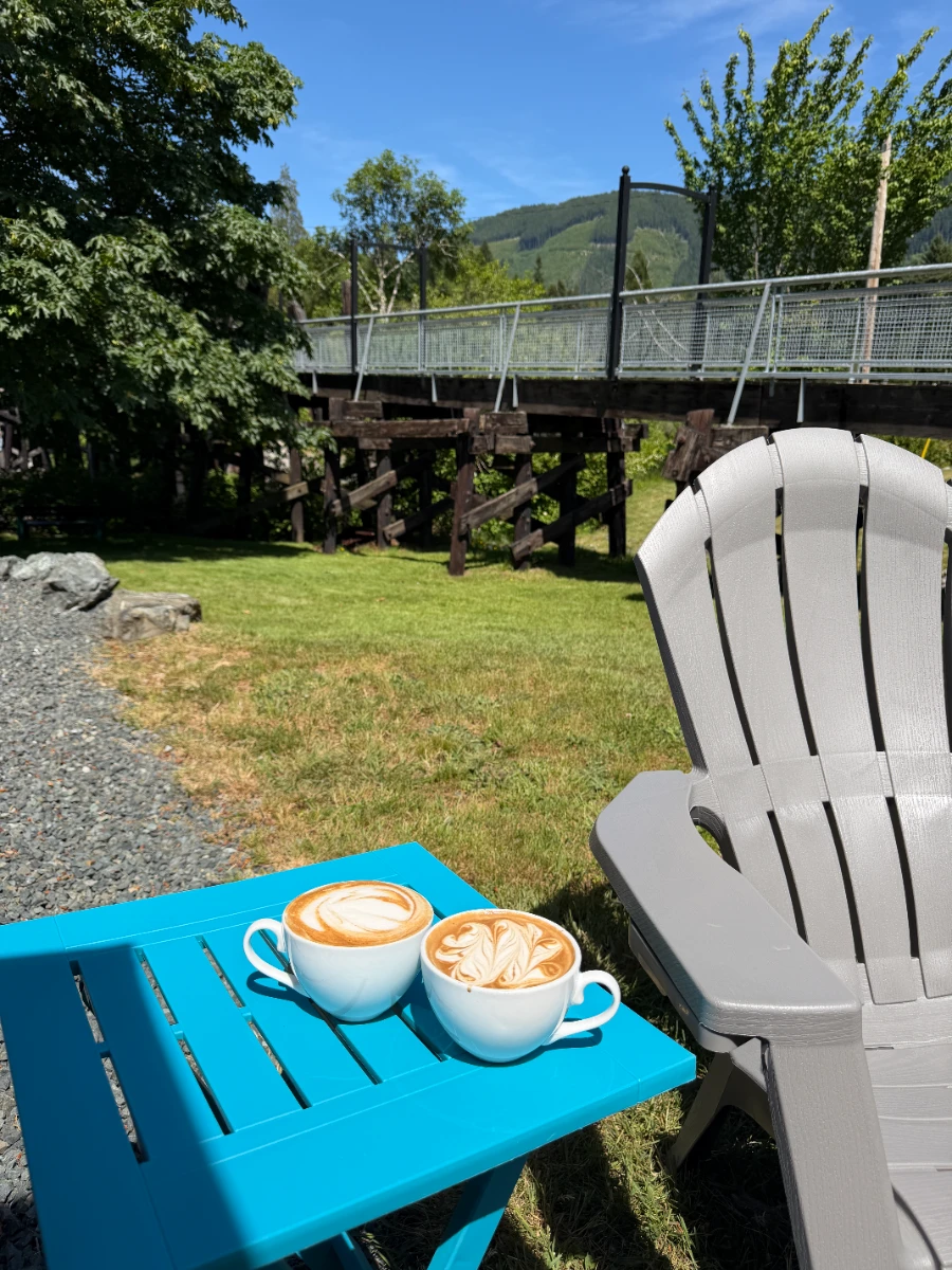 Two large lattes sit on a blue table next to a plastic Muskoka chair