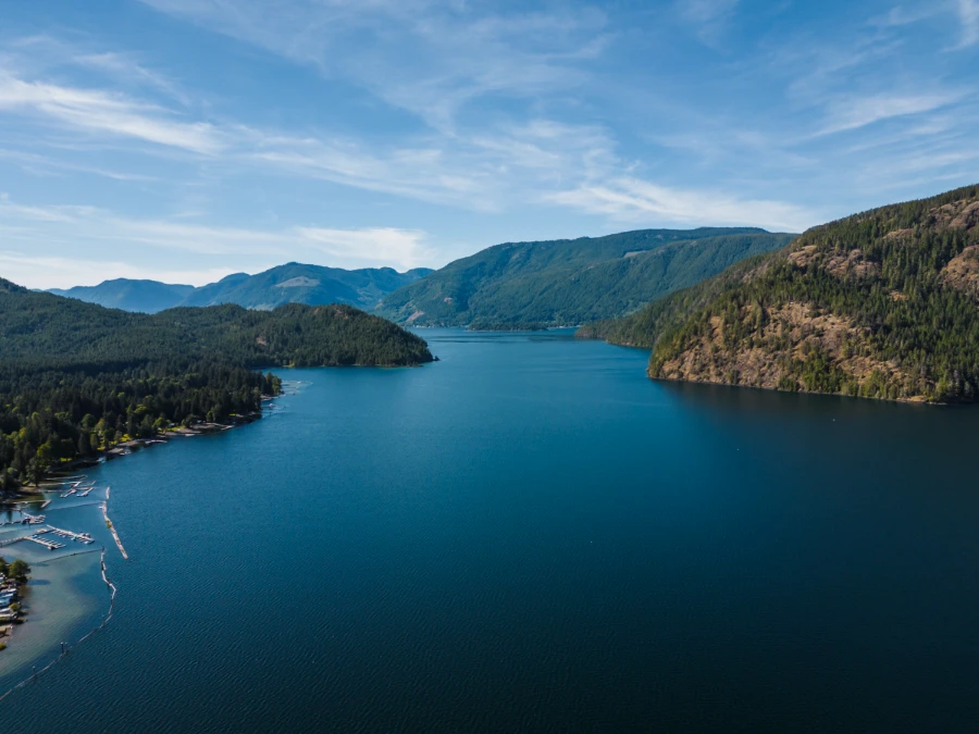 A deep blue lake lined with lush green rolling hills and shores lined with floating log barriers