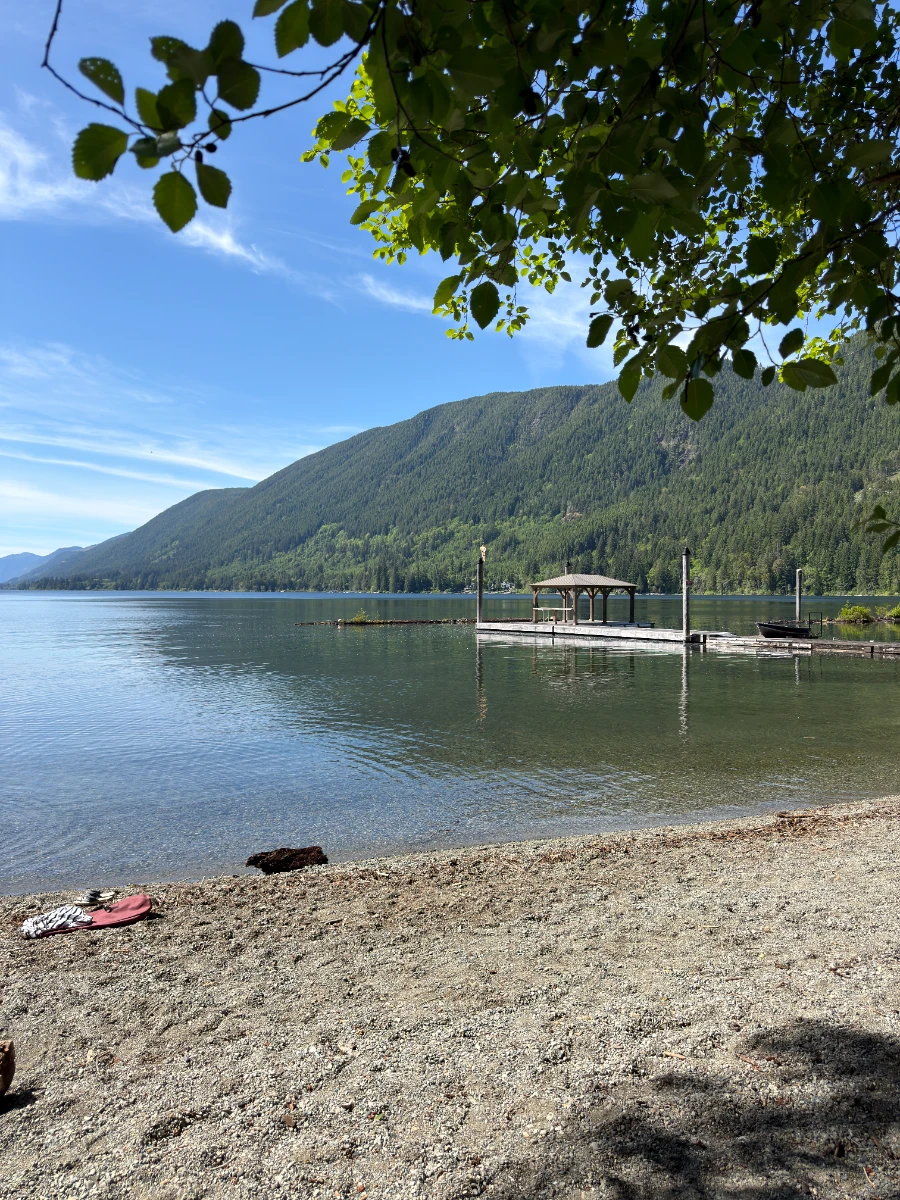 A large gravel beach on Cowichan Lake with a private dock on the water in the distance