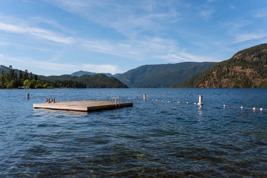 A square floating dock, floating just off the shore on Cowichan Lake, is surrounded by a floating border