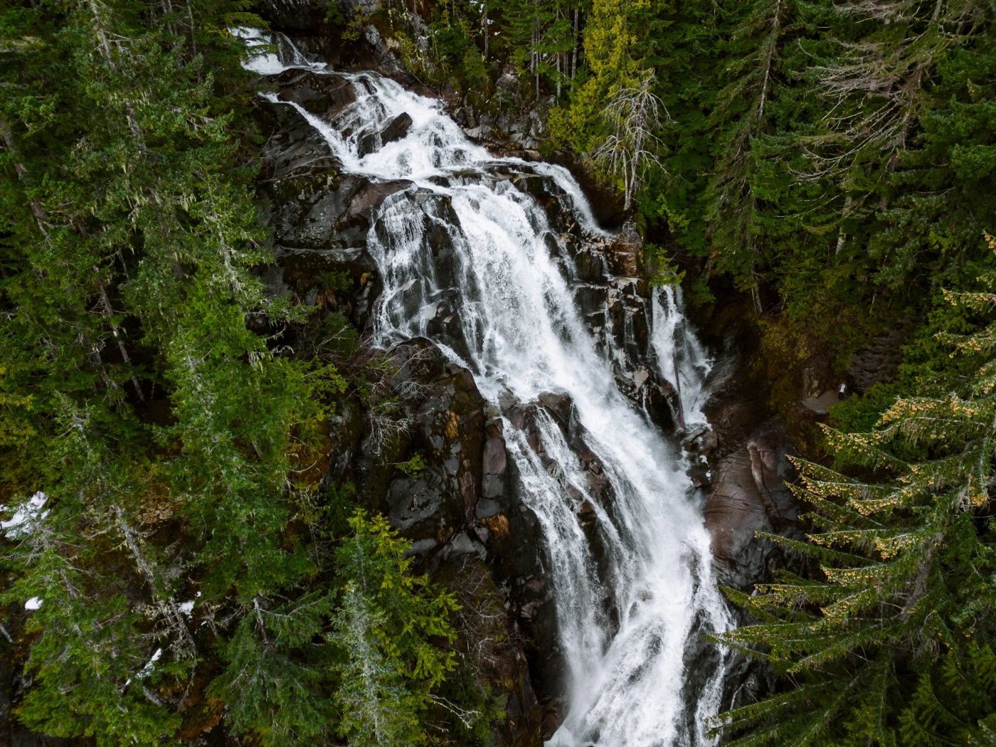 Powerful stream of water pours over a polished granite cliff and makes a sharp 90 degree turn, surrounded by lush green trees