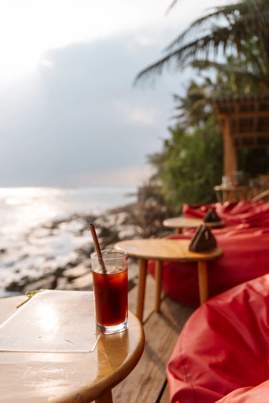 A red cocktail sitting on a wooden table alongside the beach