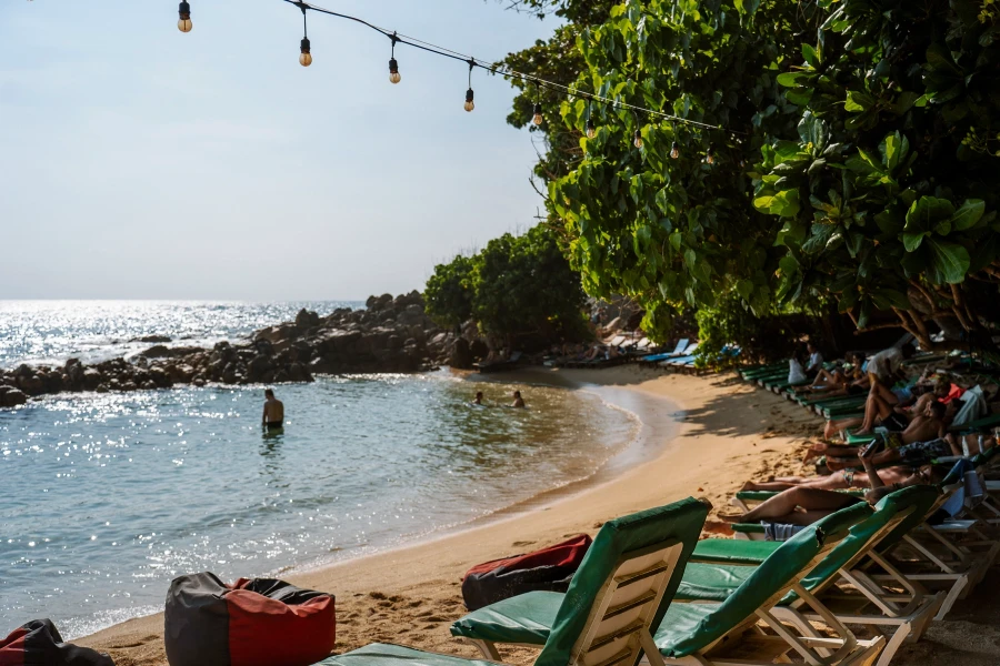 A row of plastic beach chairs line a secluded sandy beach with calm waters protected by a natural row of rocks