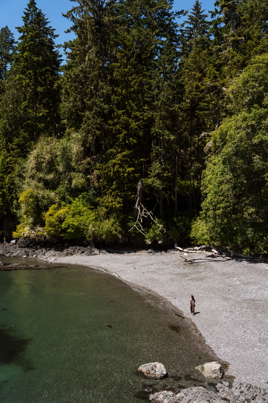 A woman walks along the shore of a small protected rocky beach in East Sook Regional Park