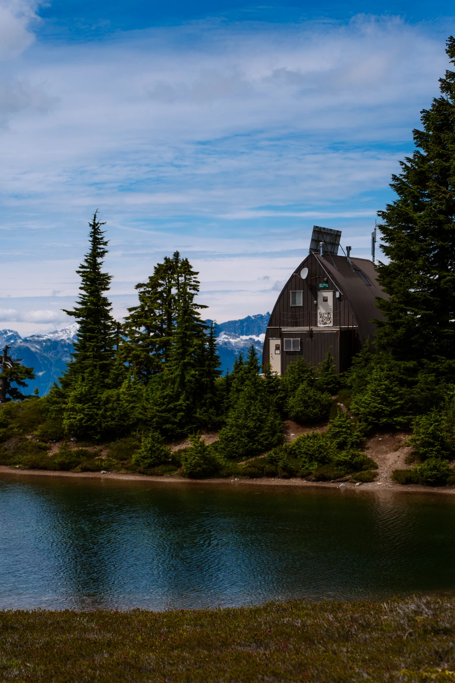A wooden A-frame shelter on the edge of an alpine lake