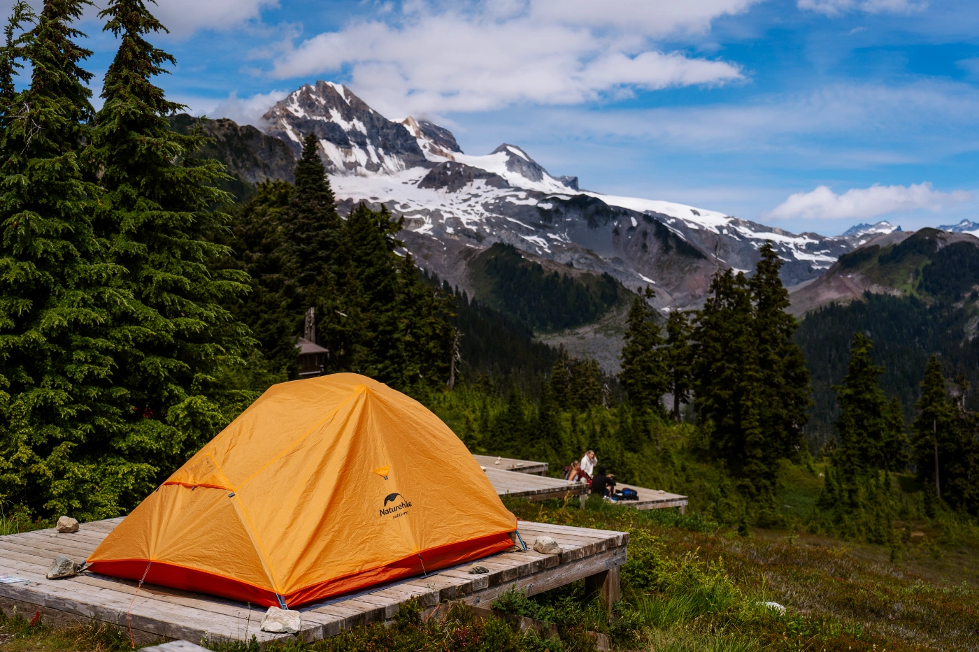 An orange Naturehike tent set up on a wooden tent pad on a mountainside surrounded by jagged mountain peaks