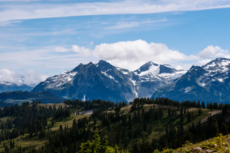 A long ridgeline stretches through the alpine with taller snow-capped mountains towering over the ridge in the distance