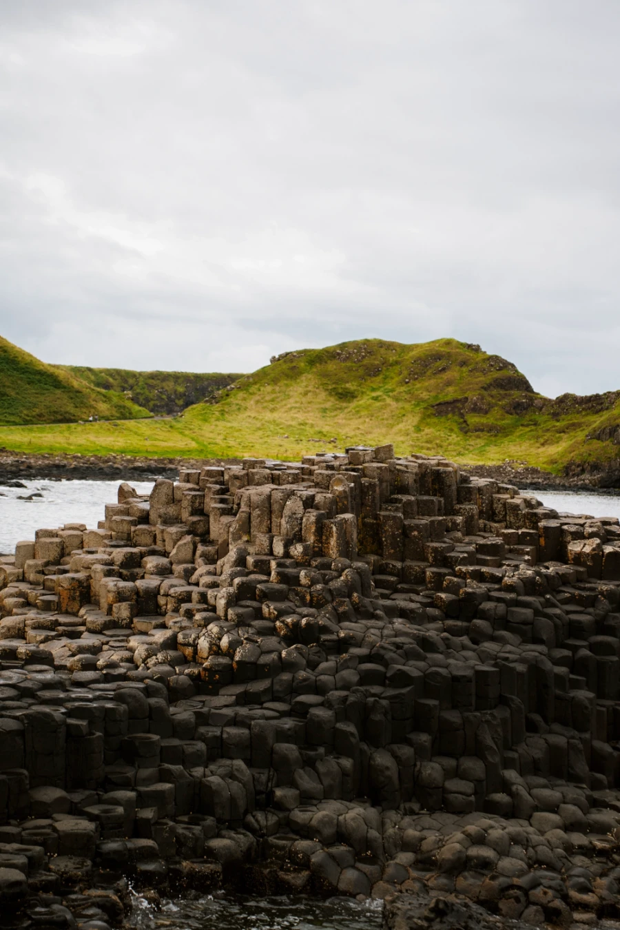 A stretch of odd hexagon shaped stone pillars form a rocky outcropt surrounded by rolling green hills
