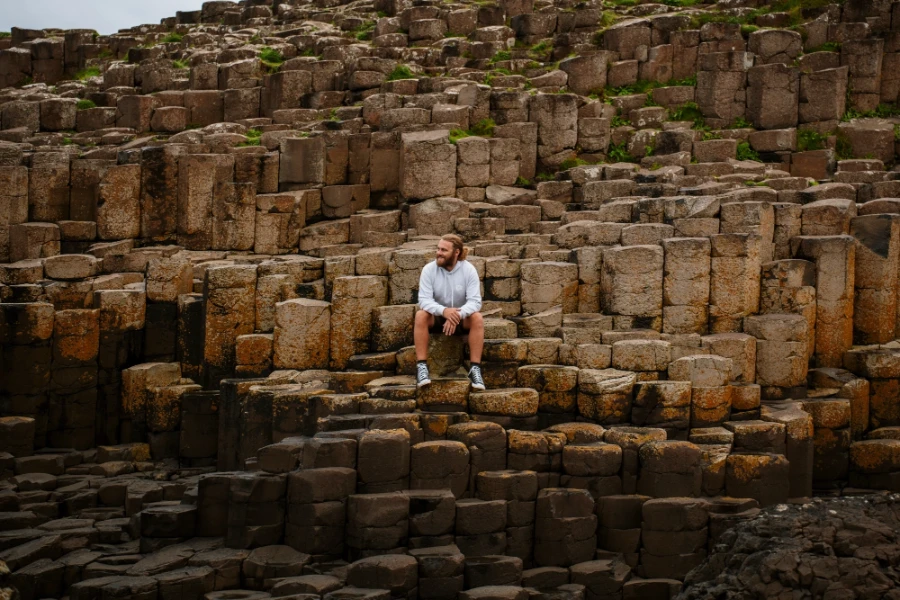 A man sits on the side of a rocky hill comprised of hundreds of hexagon-shaped pillars