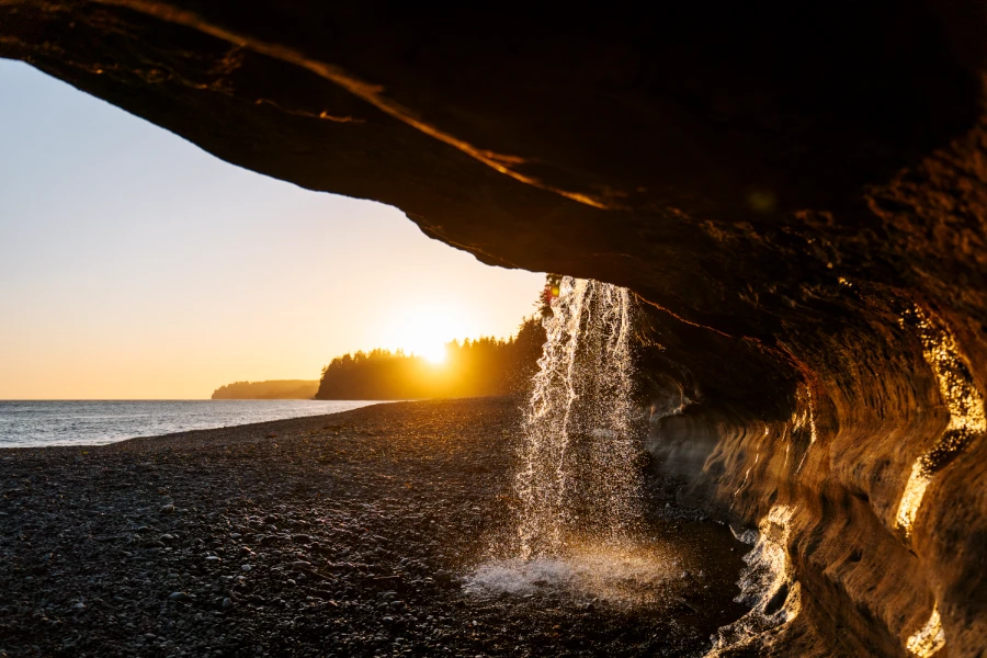 A steady stream of water pouring over a sandstone cliff onto the rocky beach below