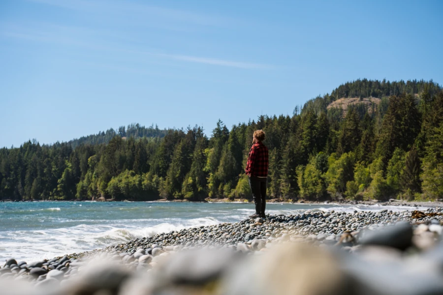 A man stands on a rocky beach looking out to a choppy sea at French Beach