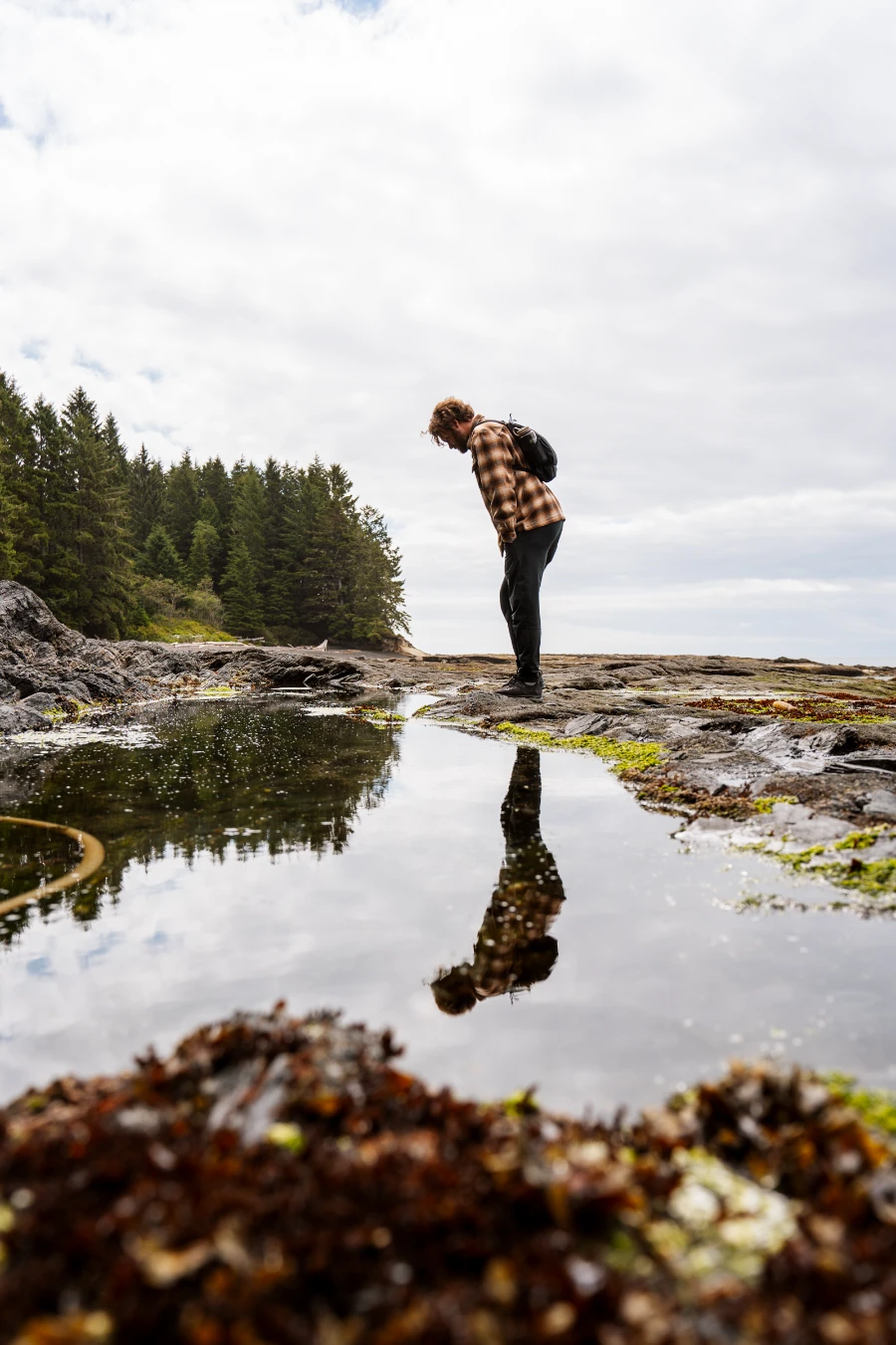A man stands above a large tidal pool at Botanical Beach with a clear reflection