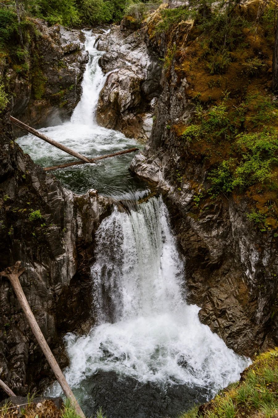 Two layers of waterfalls pour into consequtive pools, surrounded by steep cliffs and leafy green trees