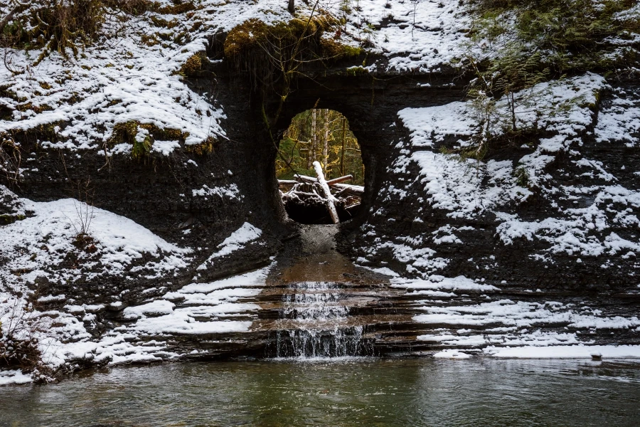 Water trickling through a large circular hole in a snow covered rock wall