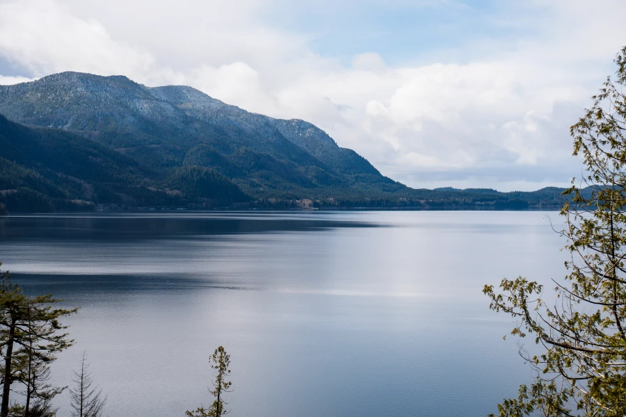 Snow and tree covered mountains tower over a massive blue lake on Vancouver Island, BC