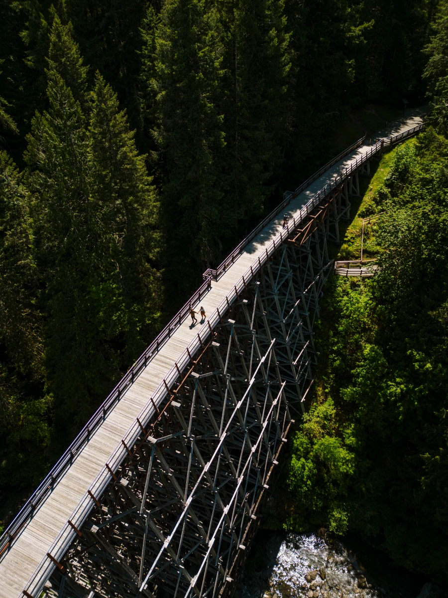 A massive wooden trestle suspends a wooden boardwalk high above a canyon