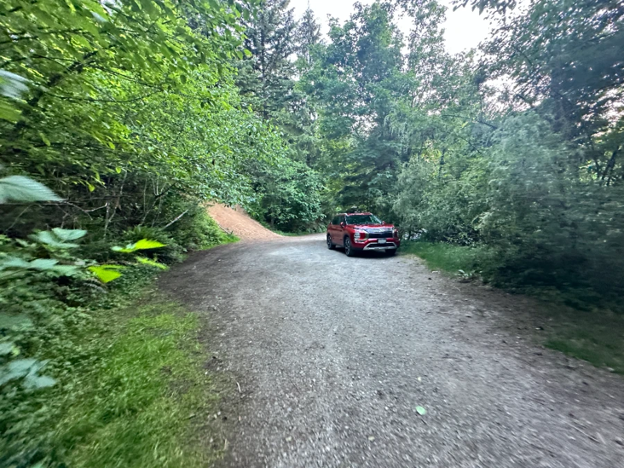 A red SUV is parked in a small gravel lot surrounded by green trees