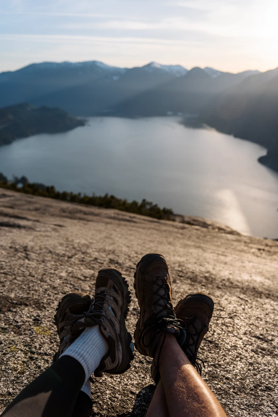 Two pairs of legs crossed over each other on the stone cliff at the top of the Stawamus Chief with the Howe Sound below.