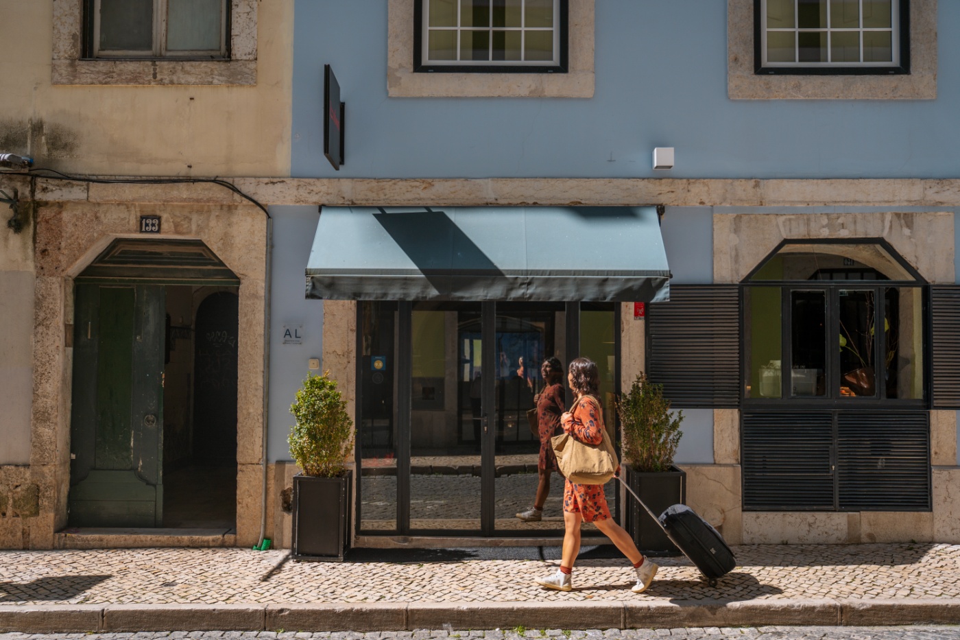 A woman walking along a cobbled sidewalk pulling her luggage in front of a European style hotel facade