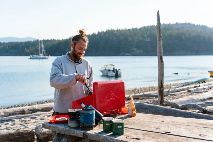 A man cooking pancakes at the campsite on Thormanby Island with anchored sailboats behind him