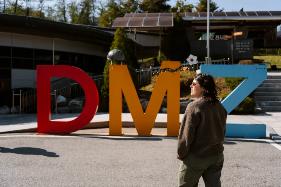 Woman stands in front of large sign spelling DMZ