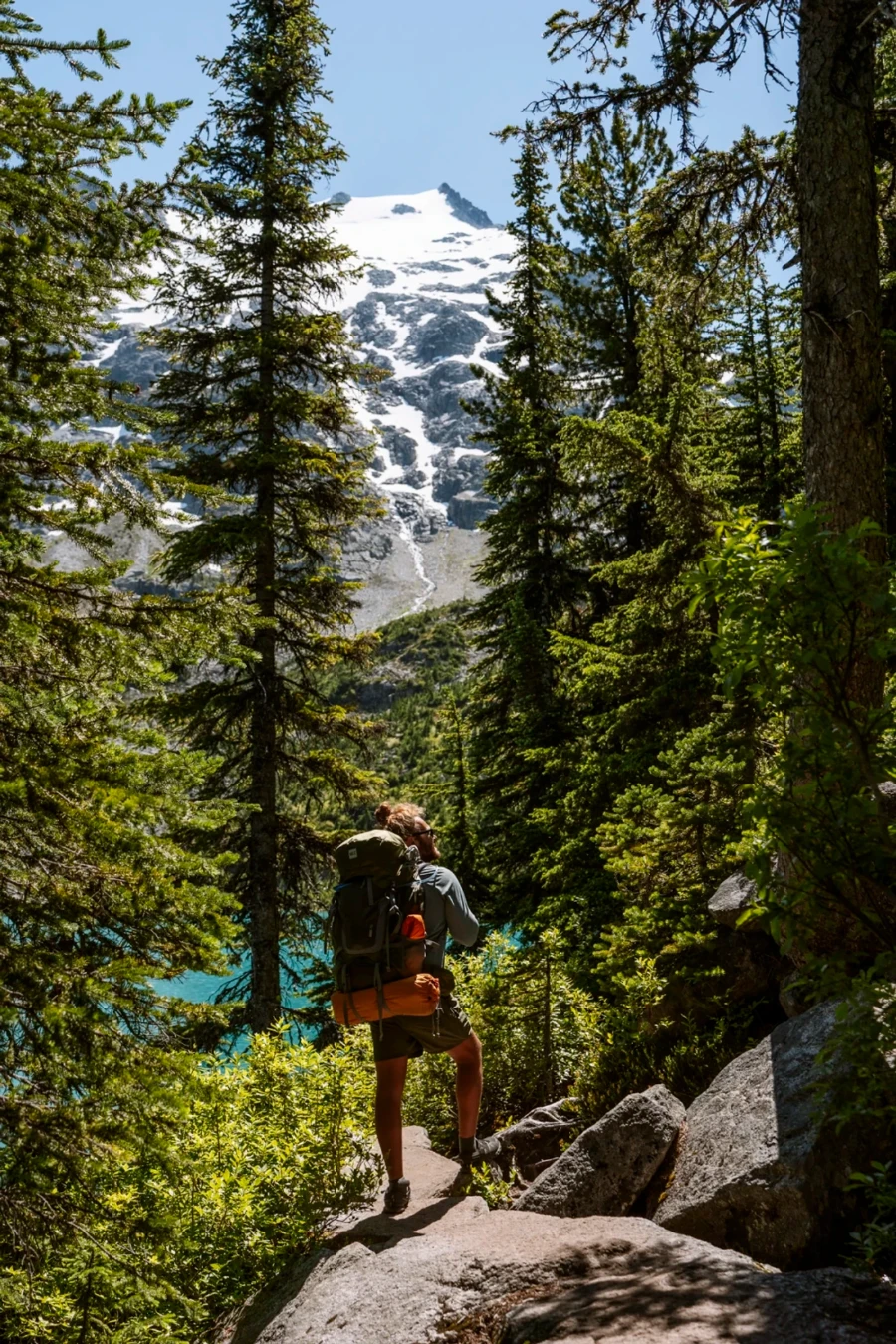 A man with a camping backpack stands on a large rock while surrounded by trees