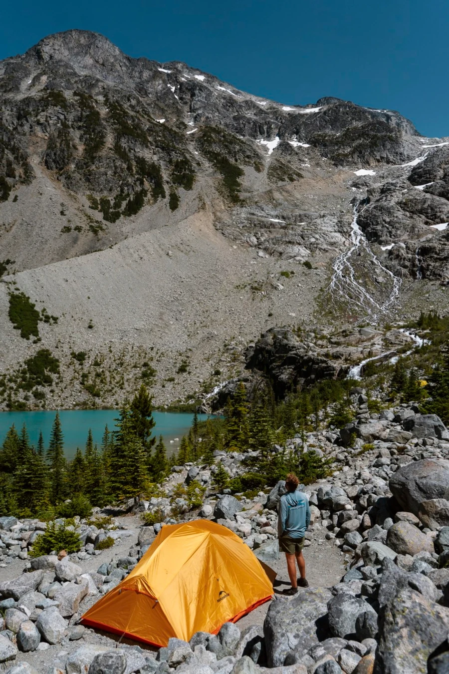 Man standing next to an orange tent at Joffre Lake Campsite surrounded by boulders