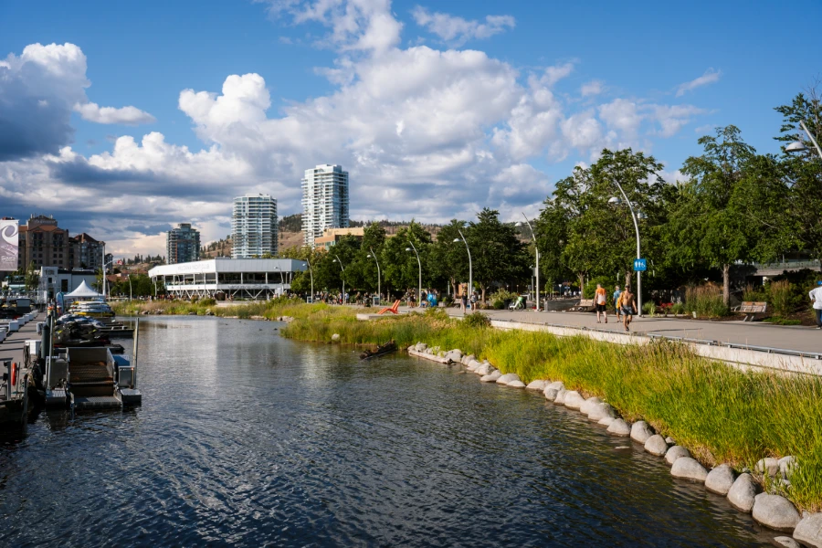 A long paved waterfront walkway stretches past the calm waters of Okanagan Lake near City Park in Kelowna