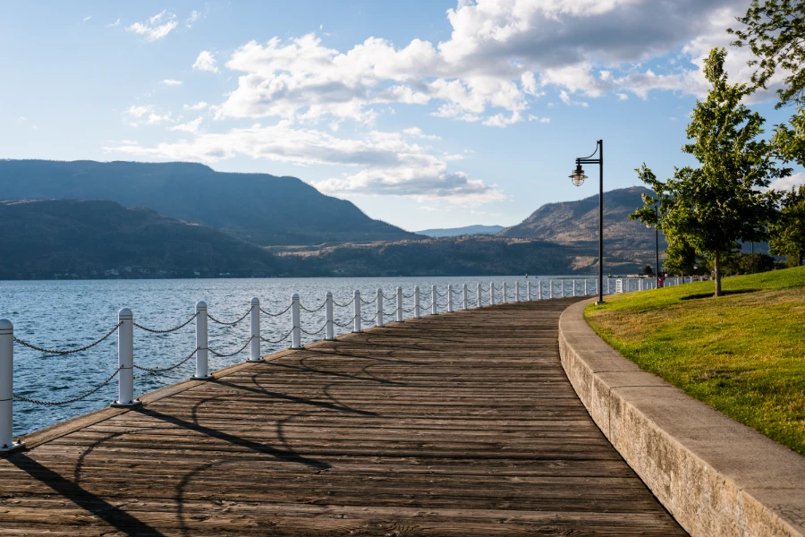 A curved wooden boardwalk winds past the calm waters of Okanagan Lake and a manicured lawn