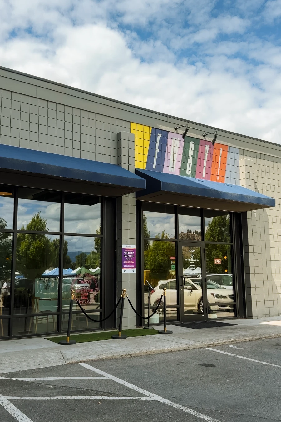 A tiled facade of a modern-looking building with tall polished windows and a stretch of turf in front with a rope barrier to form a natural que