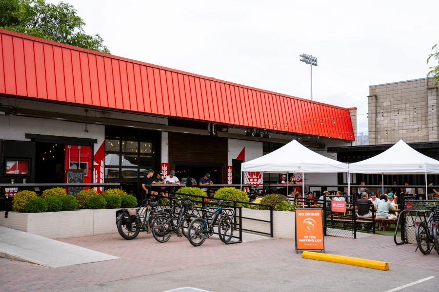Several bikes are parked, and several picnic tables are full of patrons outside the red and white painted facade of Red Bird Brewing in Kelowna