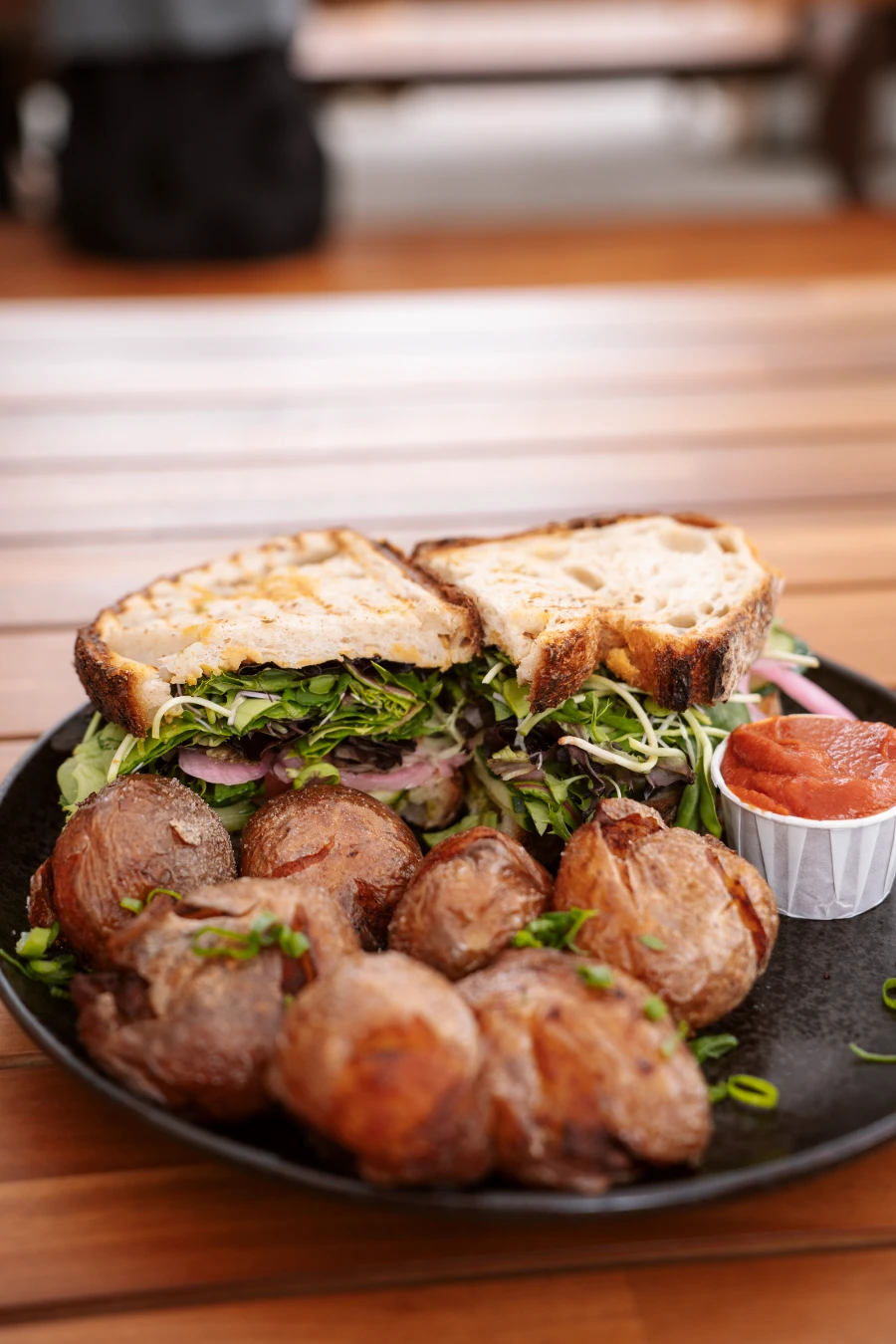 A large sandwich cut in half sits on a plate next to several well-cooked potatoes