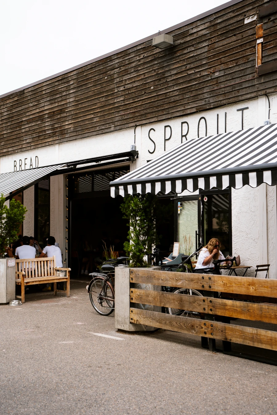 A small patio lines the facade of a white building with wooden panelling and a painted sign that reads ‘Sprout’