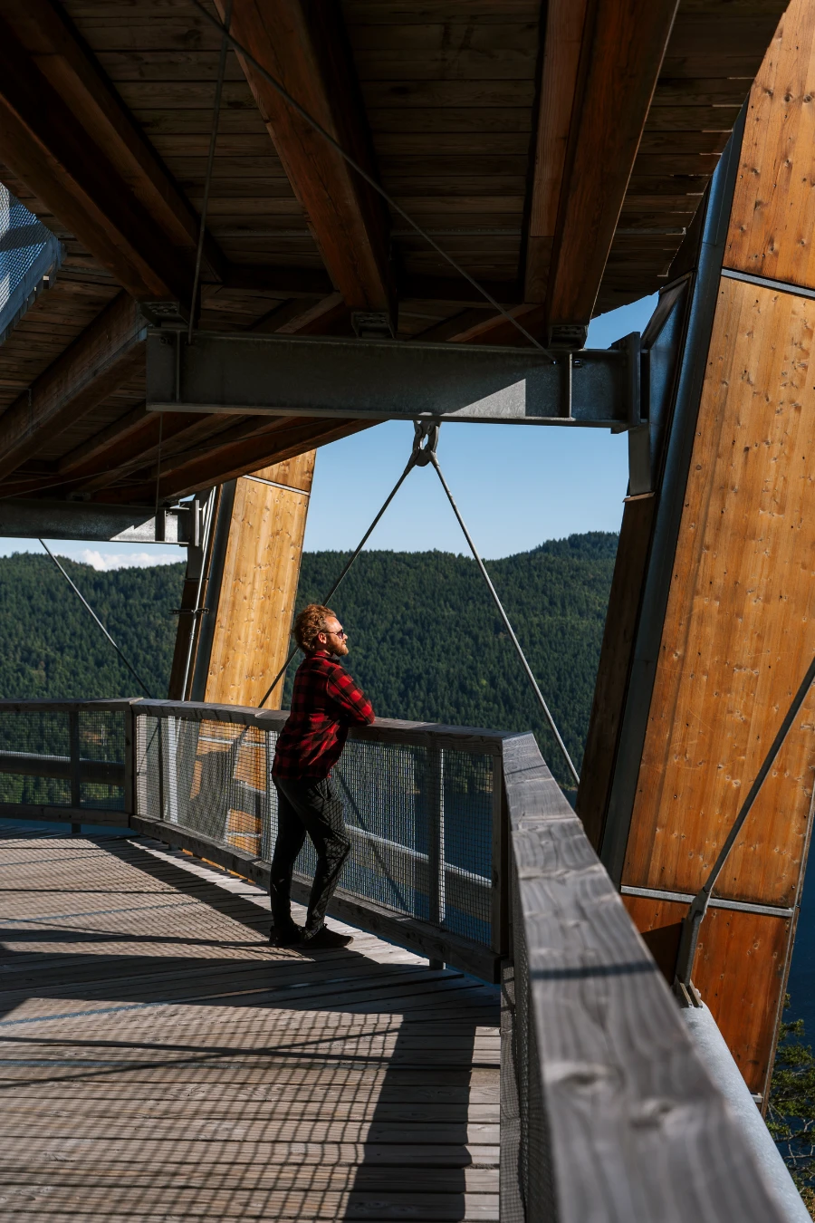 A man leans on the wooden railing that borders the spiral boardwalk on the Malahat Skywalk in Cowichan Valley