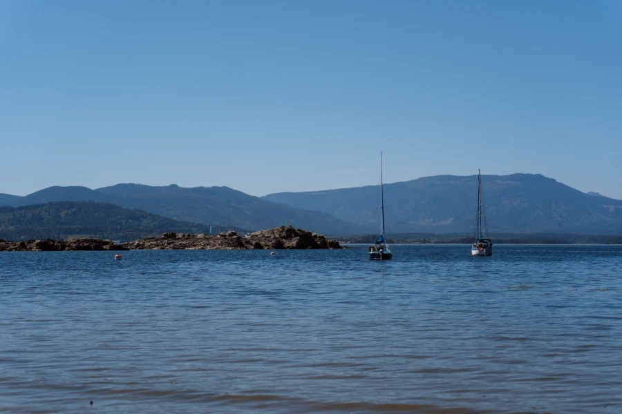 Two sailboats anchored in calm water with mountains on the horizon