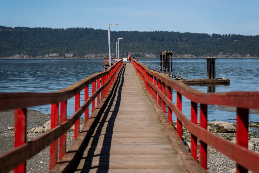 Red wooden fences lead down a wooden dock out over white sand and over blue calm waters