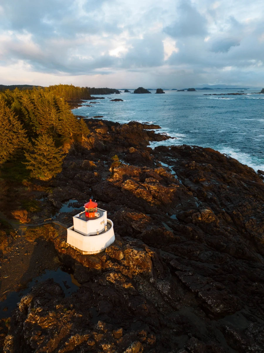 A white and red lighthouse sits on a rocky shore with a line of trees behind